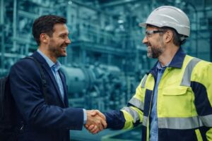 Headhunter y profesional industrial estrechándose la mano en una planta, representando la atracción de ingenieros con experiencia en un mercado industrial competitivo.